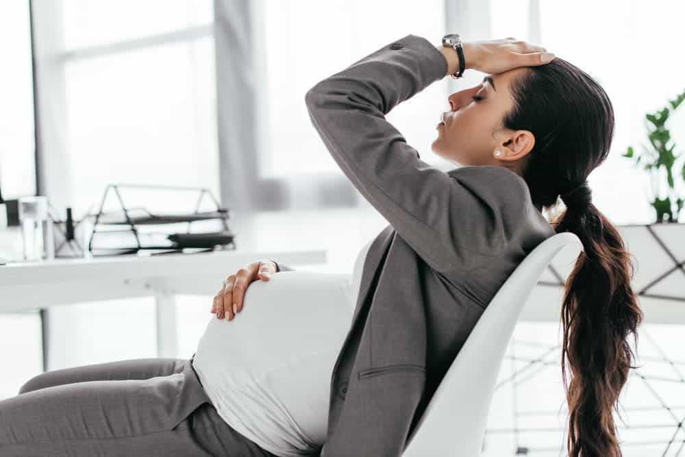 Tired pregnant woman sitting in office in chair