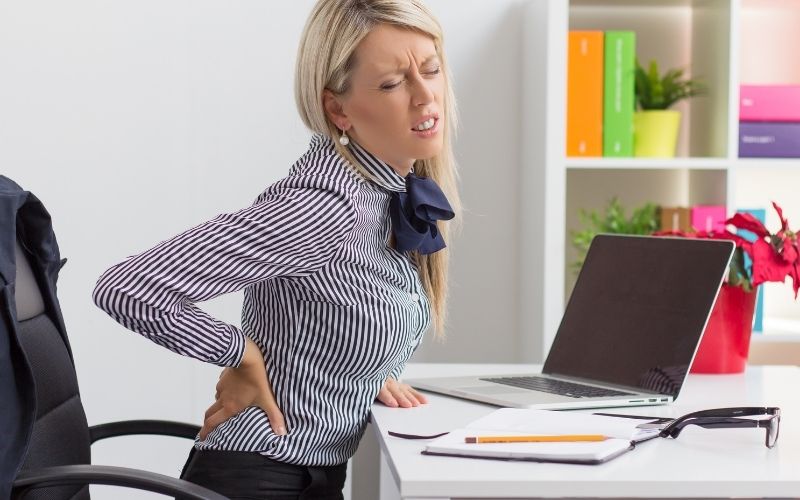 Woman has back pain during working time sitting on chair