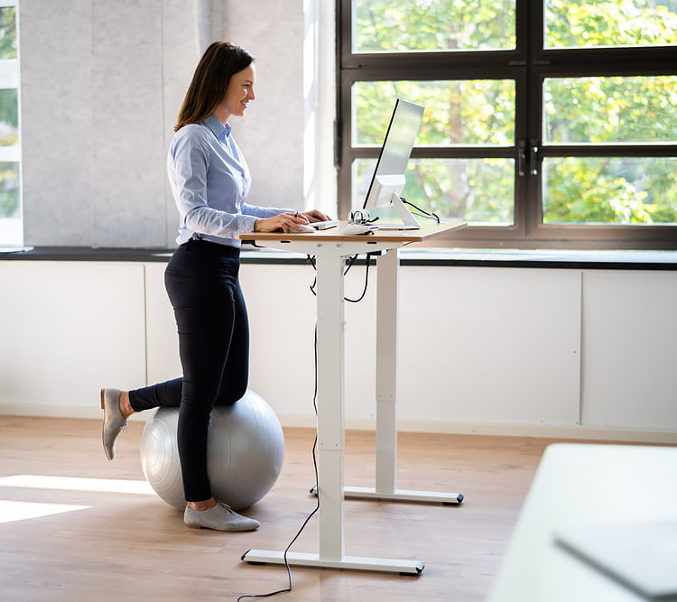 A young lady is working at her standing desk with a balance ball