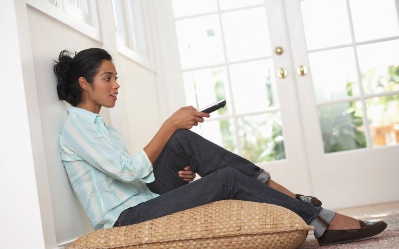 Girl sitting on cushion and using a remote control