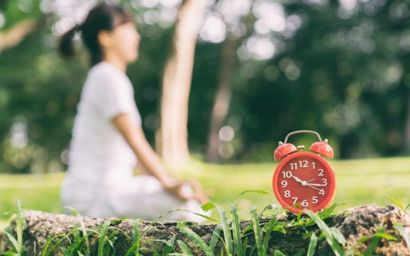 Woman meditates in the park with an alarm clock