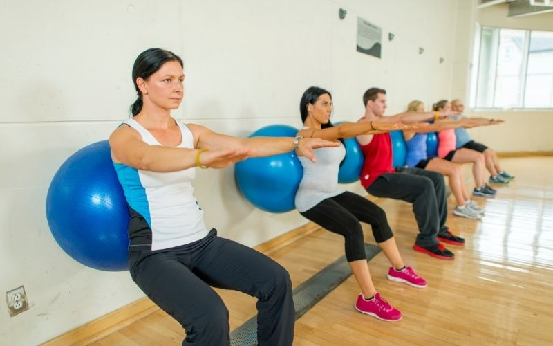 Group of people doing wall squat with exercise balls