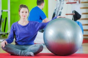 A woman sits next to an exercise ball