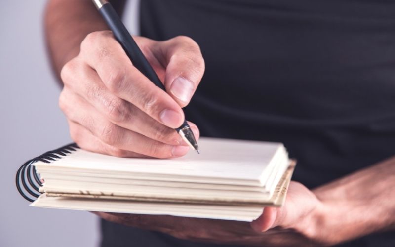 Man writing on notebook with a pencil