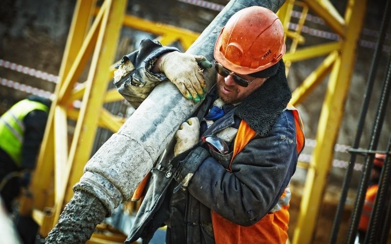 Worker at construction site carrying gray pipe